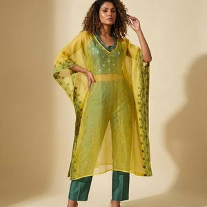 May include: A sheer yellow kaftan with dark green embroidered borders worn over a dark green sleeveless top and matching straight-leg trousers. The kaftan features wide sleeves and a V-neckline, while the undergarment has a subtle pattern.