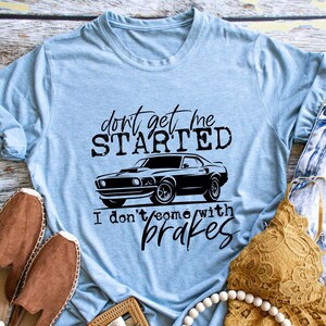 Puede incluir: Una camiseta azul claro con un gráfico negro de un coche clásico y el texto "Don't get me started I don't come with brakes".