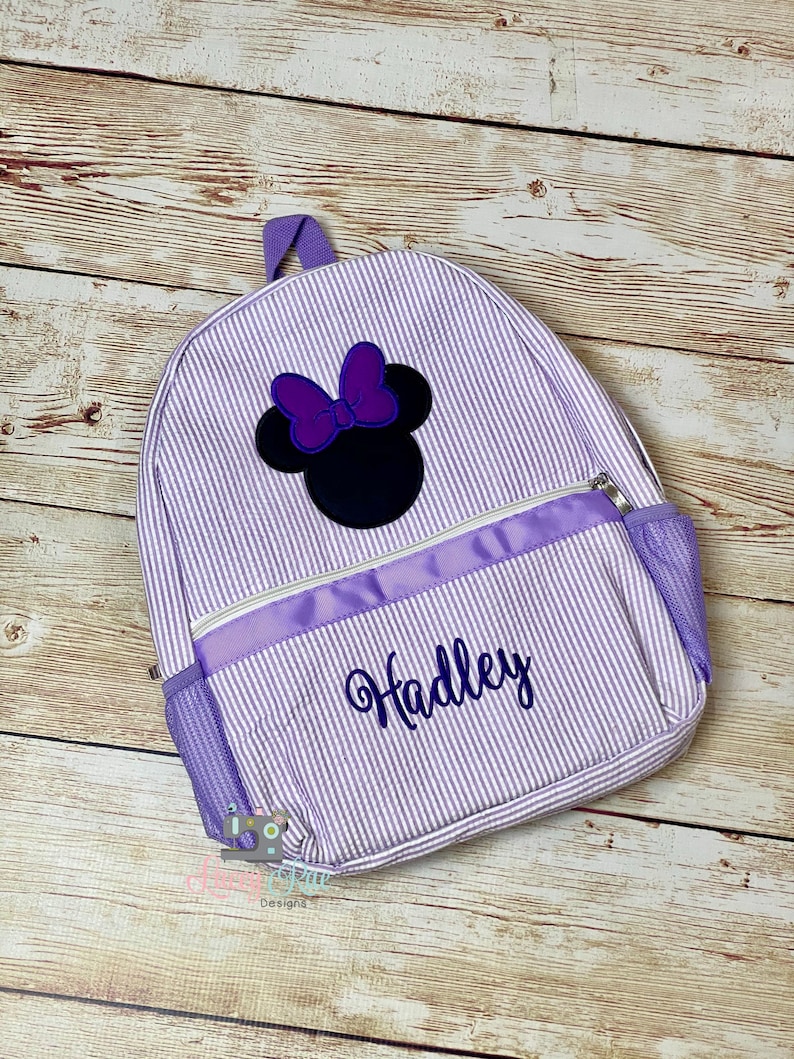 May include: Purple and white striped backpack with a black and purple Minnie Mouse applique and the name "Hadley" embroidered in purple.