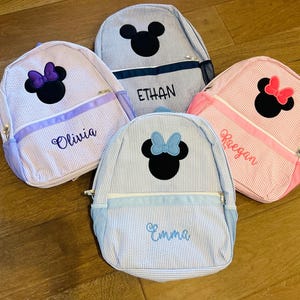 May include: Four blue and white striped Minnie Mouse backpacks with personalized names: Olivia, Ethan, Keegan, and Emma.