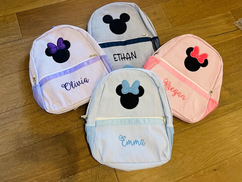 May include: Four blue and white striped Minnie Mouse backpacks with personalized names: Olivia, Ethan, Keegan, and Emma.