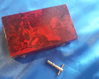 May include: A red wooden music box with a vintage image of a man in a forest setting. The box has a keyhole and a small key is included.