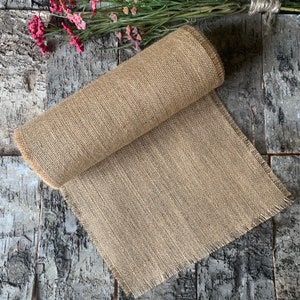 Puede incluir: Un rollo de tela de arpillera natural con un borde deshilachado. La tela est&aacute; enrollada y el extremo es visible.