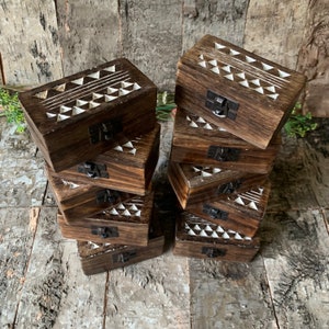 May include: A stack of eight wooden boxes with a geometric pattern carved into the top. The boxes are dark brown with white geometric designs and have a small metal latch on the front.