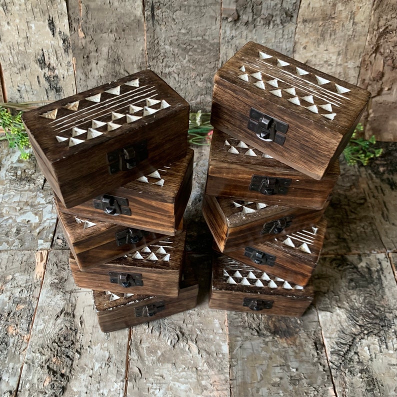 May include: A stack of eight wooden boxes with a geometric pattern carved into the top. The boxes are dark brown with white geometric designs and have a small metal latch on the front.