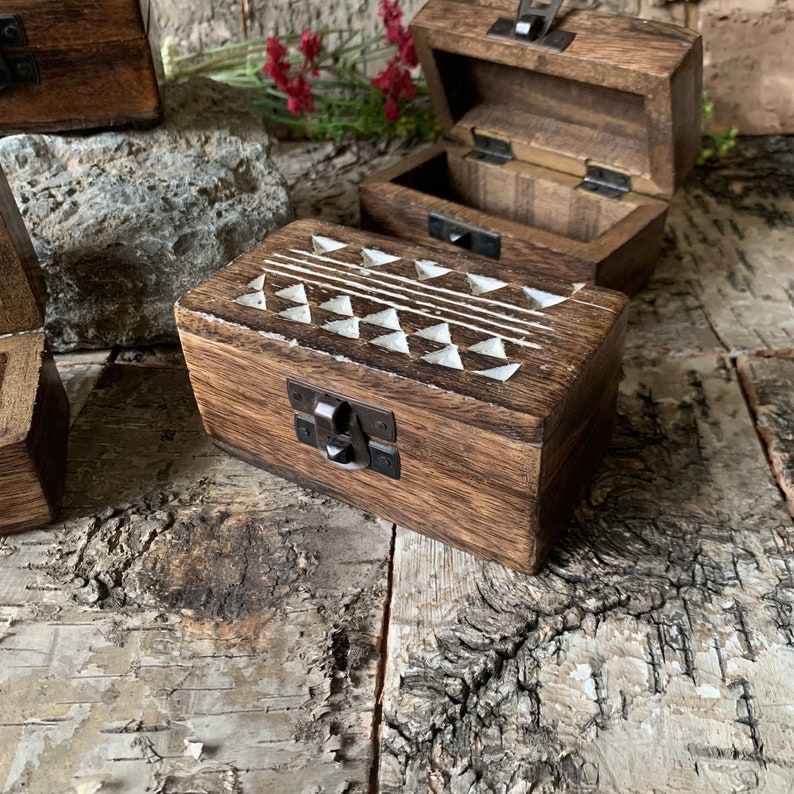 May include: A small wooden box with a hinged lid and a carved geometric pattern on the top. The box has a dark brown stain and a metal latch.