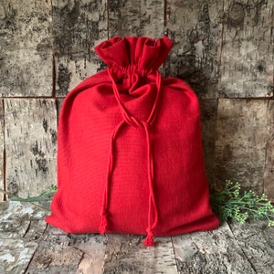 May include: A red fabric drawstring bag with a gathered top and a rope closure. The bag is sitting on a wooden surface.