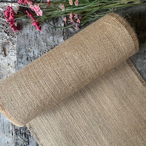 Puede incluir: Un rollo de tela de arpillera marr&oacute;n natural con un borde deshilachado. La tela est&aacute; tejida con una textura apretada y uniforme.