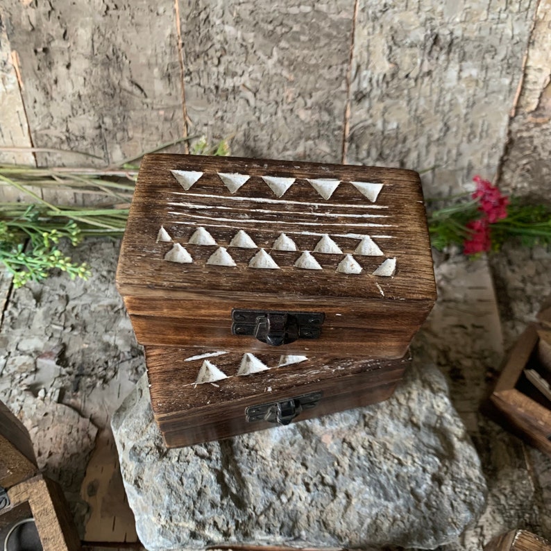 May include: A wooden box with a geometric pattern carved into the lid. The box is made of dark wood and has a white geometric pattern carved into the lid. The box is closed and has a metal latch.