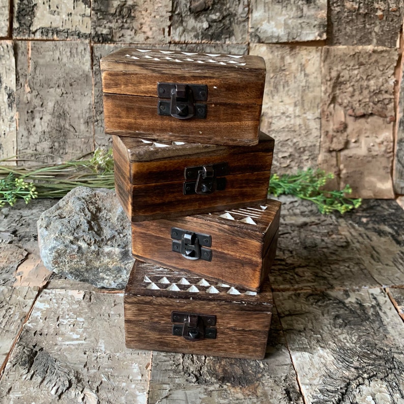 May include: Four wooden boxes stacked on top of each other. The boxes are all brown and have a white geometric pattern on the top. Each box has a black metal latch.