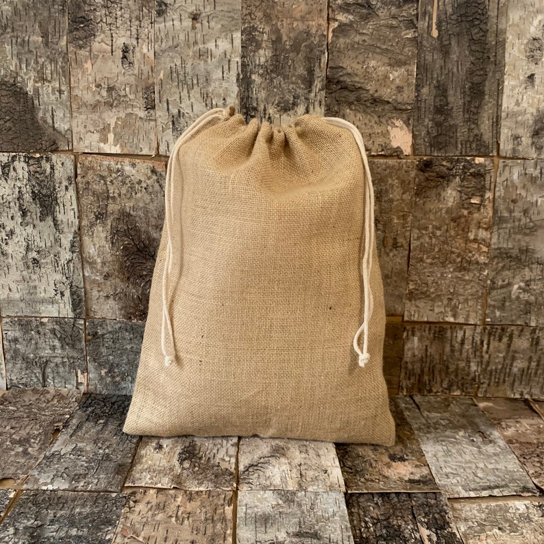 Pode incluir: Uma bolsa bege de juta com fecho de cord&atilde;o branco. A bolsa &eacute; feita de um material grosso e tecido e est&aacute; cheia. O fundo &eacute; uma parede com pain&eacute;is de madeira.