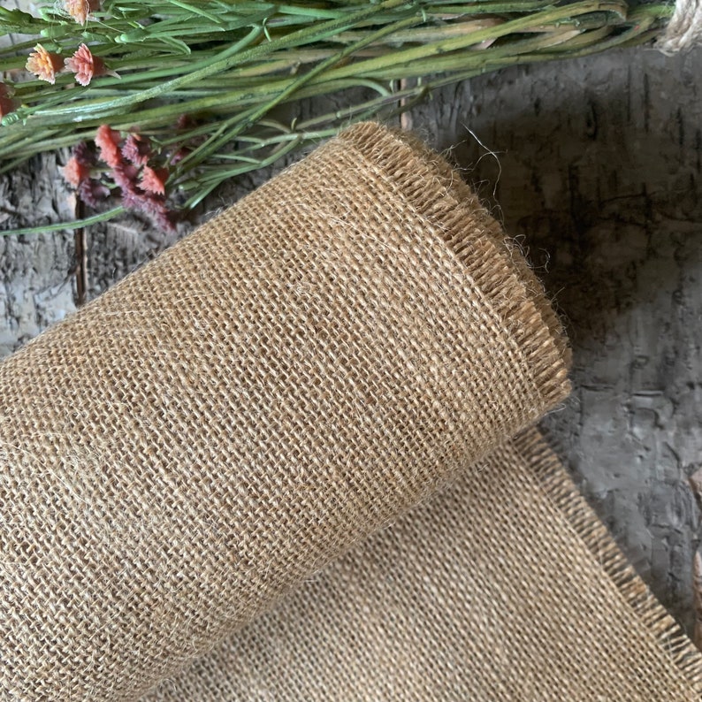 Puede incluir: Un rollo de tela de arpillera marr&oacute;n natural con un borde deshilachado. La tela est&aacute; tejida con un tejido apretado y uniforme.