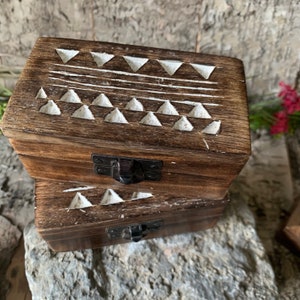 May include: Two wooden boxes with a white geometric pattern carved into the top. The boxes have a latch on the front and are stacked on top of each other.