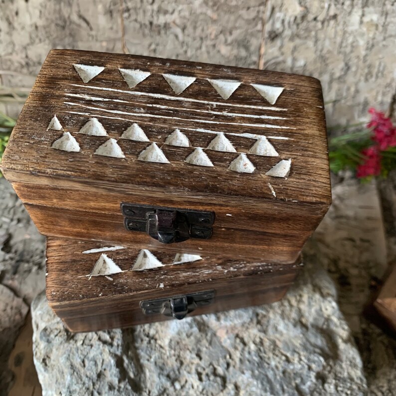 May include: Two wooden boxes with a white geometric pattern carved into the top. The boxes have a latch on the front and are stacked on top of each other.
