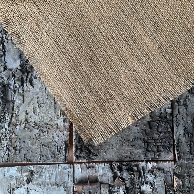 Puede incluir: Primer plano de un trozo de tela de arpillera con un borde deshilachado, que se encuentra sobre un trozo de madera con una superficie rugosa y texturizada.