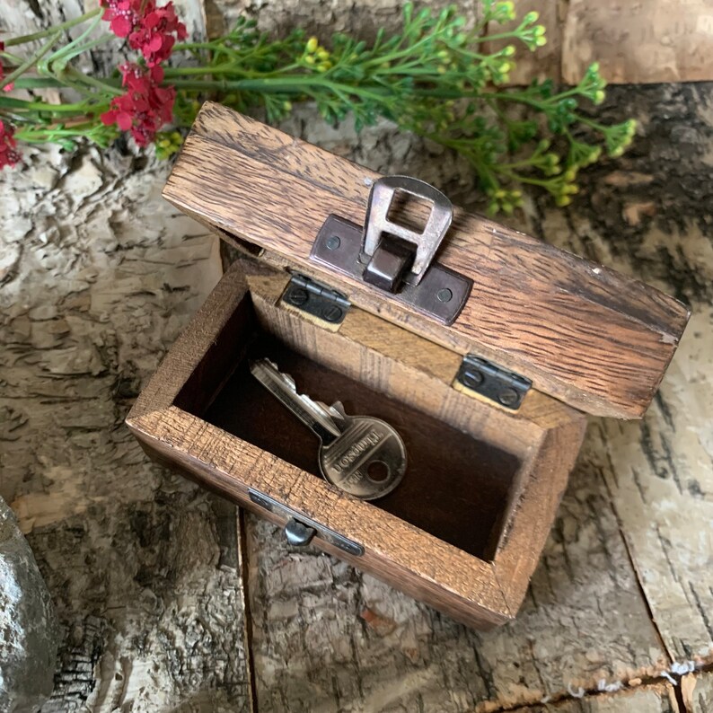 May include: A wooden box with a hinged lid and a metal latch. The box is open and a key is inside. The box has a dark brown stain and a wood grain pattern.