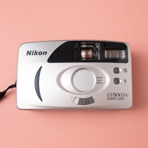 May include: A silver Nikon EF500SV Quartz Date camera with a black strap. The camera has a black lens with a 28mm lens.