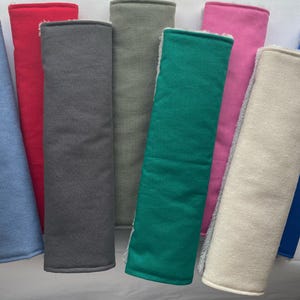 May include: A selection of rectangular fabric items in various colours, including blue, red, grey, green, pink, and beige. Each item has a contrasting border and a soft, textured appearance, suggesting a comfort-focused design.