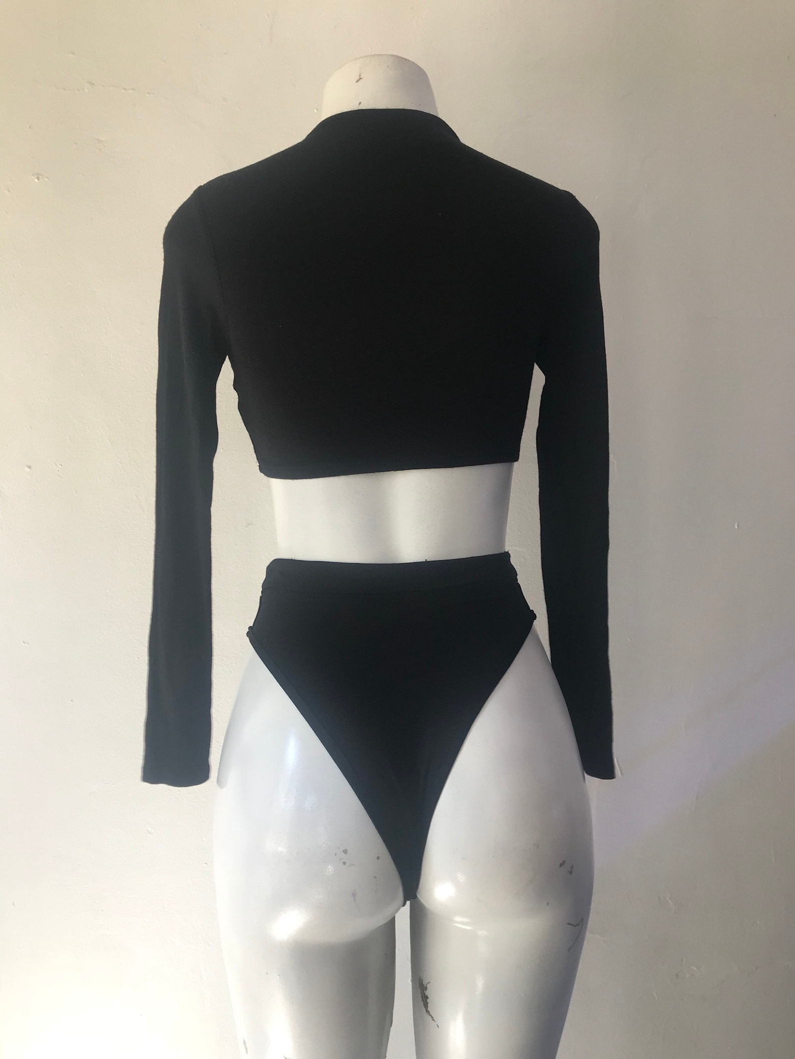 Back view of black two-piece swimsuit with long sleeve crop top and high-cut high-waisted bottoms on mannequin.