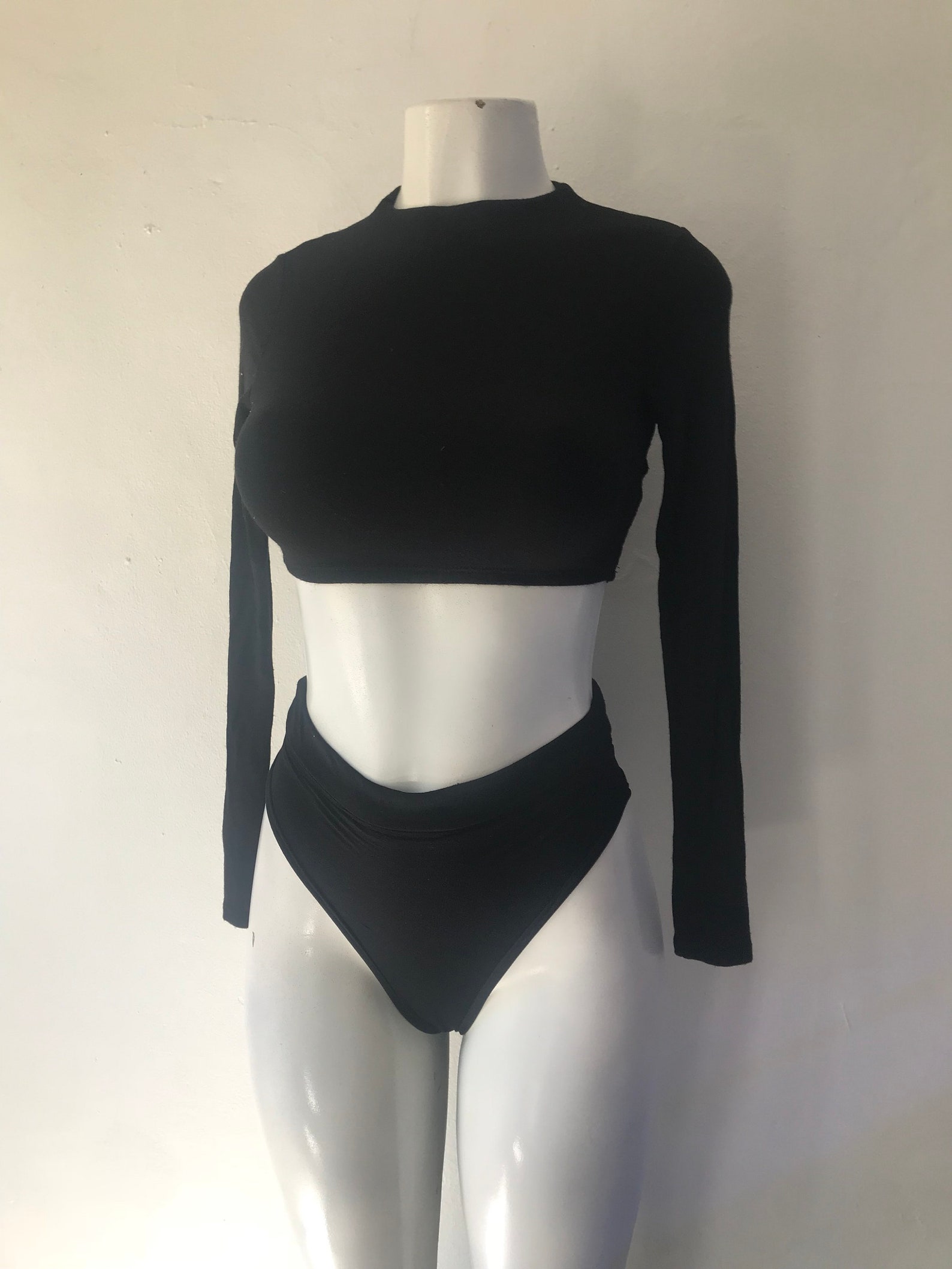 Black two-piece swimsuit with a long sleeve crop top and high-waisted bottom on mannequin.