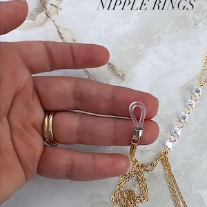 May include: A close-up of a gold chain with a clear plastic ring attached. The chain is made of multiple strands of different thicknesses. The ring has a small loop at the top. The text "NEW NON PIERCED NIPPLE RINGS" is visible at the top of the image.