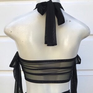 May include: Black mesh halter top with a tie at the back of the neck. The top has a layered design and is made of a sheer fabric.