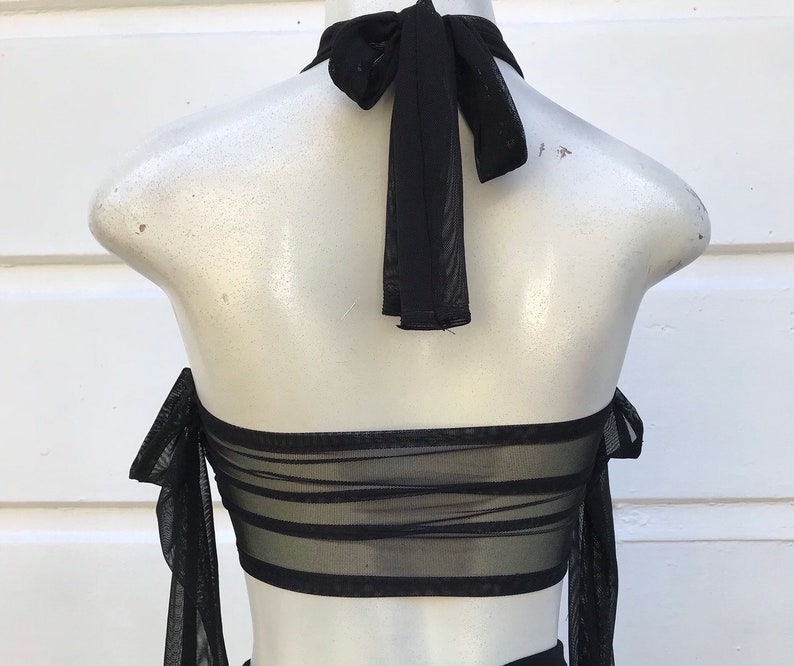 May include: Black mesh halter top with a tie at the back of the neck. The top has a layered design and is made of a sheer fabric.