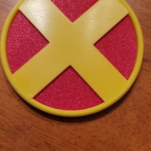 May include: A yellow X-shaped design on a red circular background. The design is raised and has a textured surface.