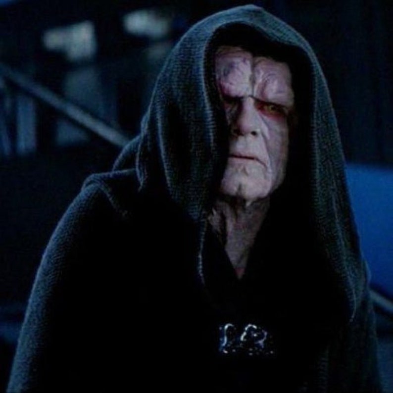 Pode incluir: Um close-up de um personagem da franquia Star Wars vestindo uma t&uacute;nica escura com capuz. O personagem tem pele p&aacute;lida e olhos vermelhos.