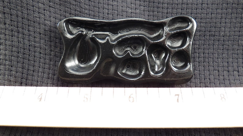 Pode incluir: Um molde de pl&aacute;stico preto com um design em relevo da palavra "Ore" em uma fonte estilizada. O molde mede aproximadamente 12,7 cm de comprimento e 5 cm de largura.