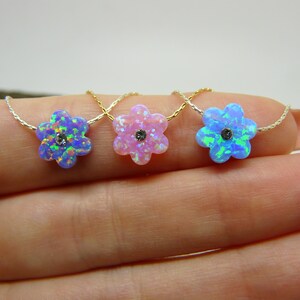 Puede incluir: Tres collares con colgantes en forma de flor. Cada colgante es de un color diferente: azul, rosa y azul-verdoso. Los colgantes florales tienen una peque&ntilde;a piedra oscura en el centro y est&aacute;n ensartados en delicadas cadenas de oro y plata.