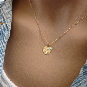 May include: A gold necklace with a hammered disc pendant and a small turquoise bead. The necklace is on a model wearing a denim jacket.