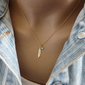 May include: A gold chain necklace with a small turquoise bead and a gold feather charm.
