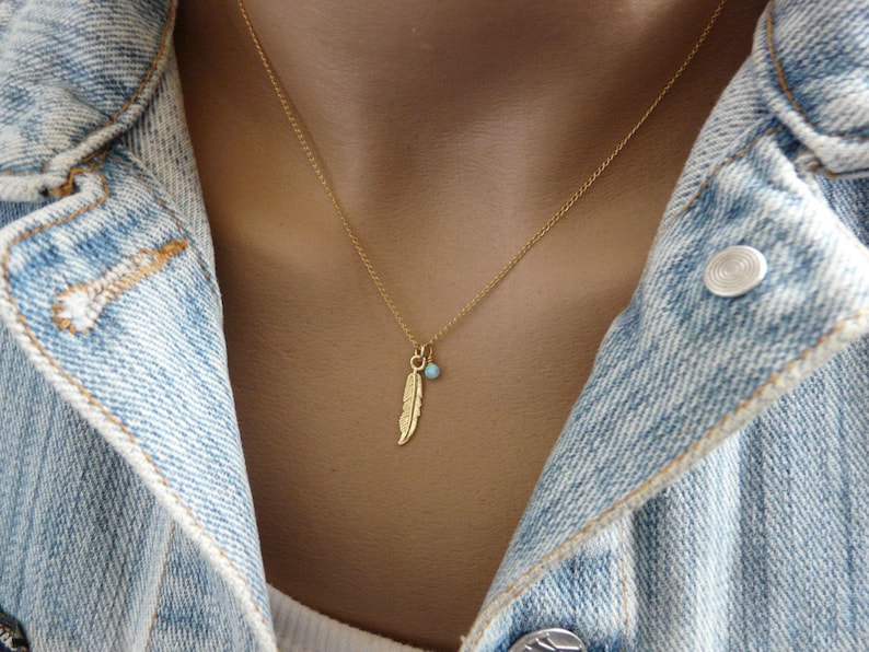 May include: A gold chain necklace with a small turquoise bead and a gold feather charm.