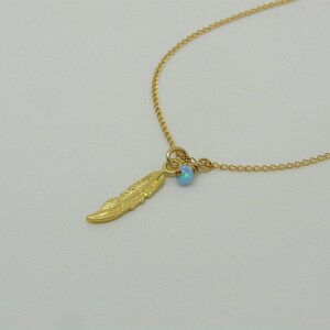 May include: A gold chain necklace with a small blue opal gemstone and a gold feather charm.