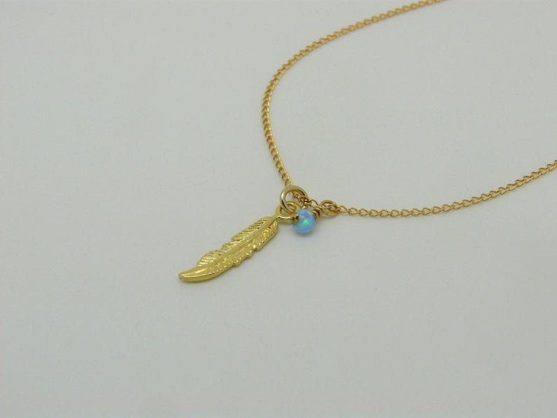 May include: A gold chain necklace with a small blue opal gemstone and a gold feather charm.