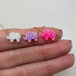 May include: A gold chain necklace with four opal elephant charms. The elephants are in white, lavender, and pink.