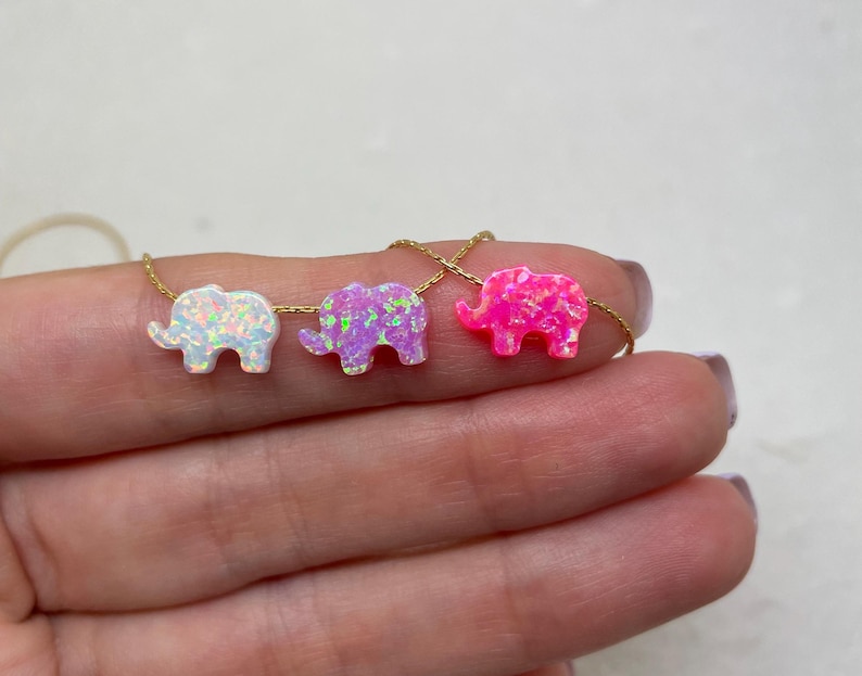 May include: A gold chain necklace with four opal elephant charms. The elephants are in white, lavender, and pink.