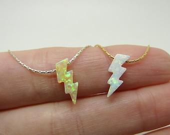 May include: Two silver and gold necklaces with opal lightning bolt pendants. The necklaces are on a hand.