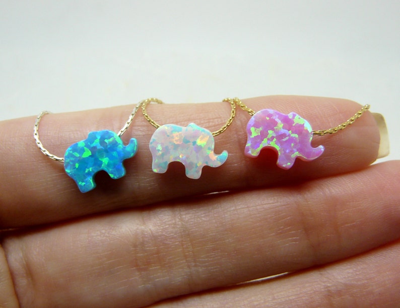 May include: Three gold necklaces with opal elephant pendants. The elephants are in shades of blue, white, and pink.