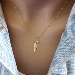 May include: A gold chain necklace with a small blue gemstone and a gold feather pendant.
