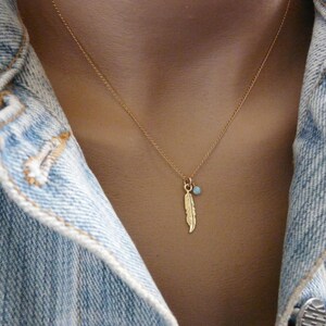 May include: A gold necklace with a delicate feather charm and a small blue gemstone pendant.