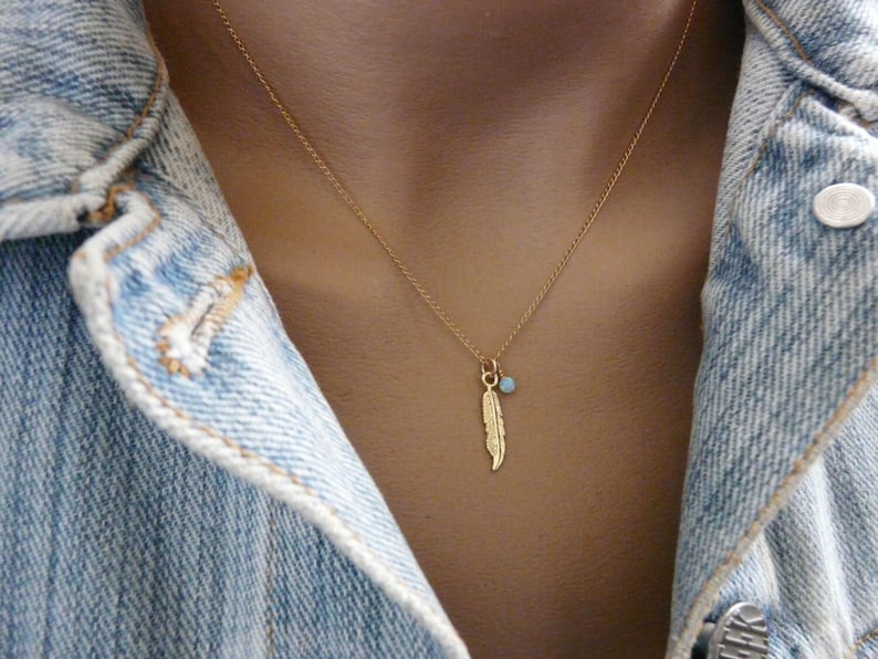 May include: A gold necklace with a delicate feather charm and a small blue gemstone pendant.