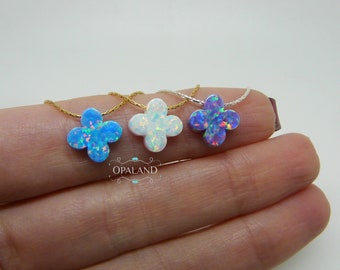 May include: Three opal clover necklaces in blue, white, and purple. Each pendant is a four-leaf clover shape, suspended on delicate gold and silver chains. The opal stones have an iridescent quality. The necklaces are displayed on a light background.