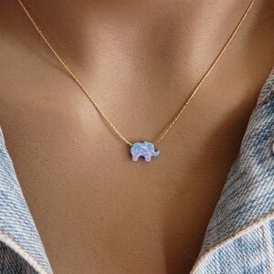 May include: A gold chain necklace with a small, blue and pink opal elephant pendant.