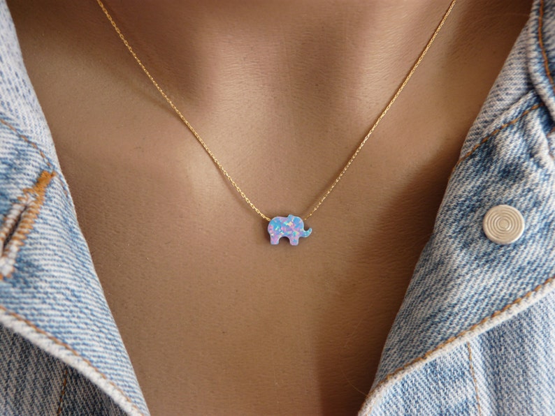 May include: A gold chain necklace with a small, blue and pink opal elephant pendant.