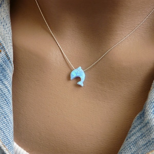 May include: A silver chain necklace with a light blue opal dolphin pendant.