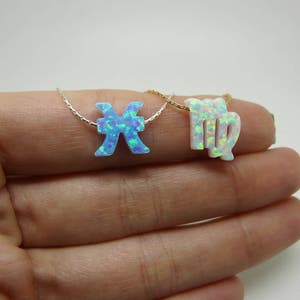 K&ouml;nnte beinhalten: Zwei silberne Halsketten mit Opal-Sternzeichen. Die Halskette links hat ein blaues Opal-Fischzeichen. Die Halskette rechts hat ein wei&szlig;es Opal-Jungfrauzeichen.