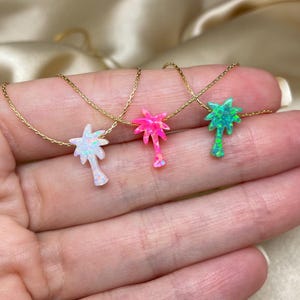 以下が含まれることがあります： オパール製のヤシの木のペンダントがついたゴールドネックレスが3本。ヤシの木は白、ピンク、緑です。
