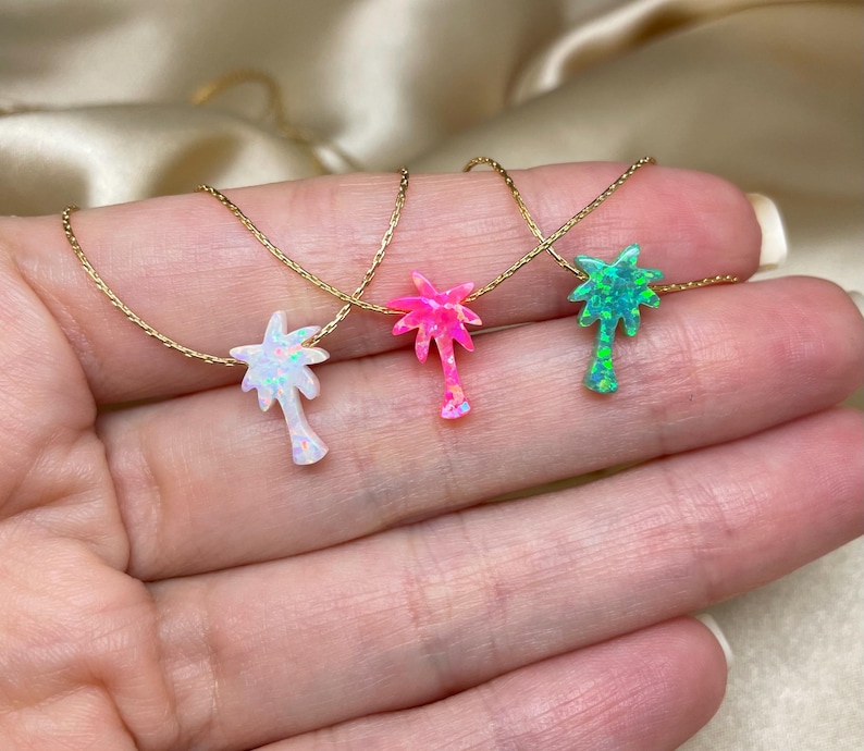 以下が含まれることがあります： オパール製のヤシの木のペンダントがついたゴールドネックレスが3本。ヤシの木は白、ピンク、緑です。